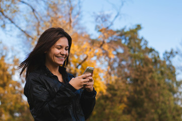 Smiling woman using mobile phone in park during the autumn.