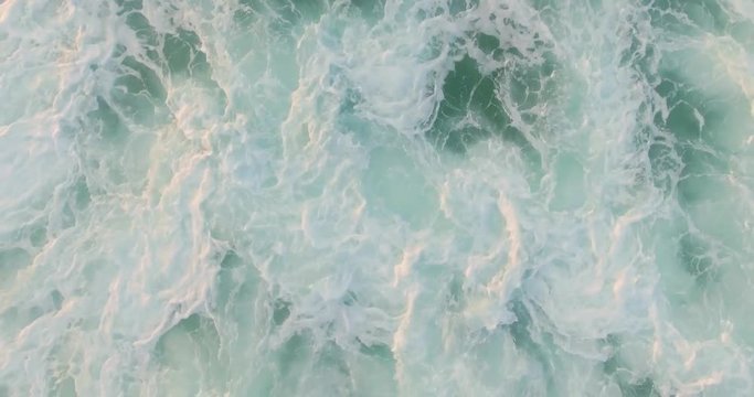 Aerial drone footage of huge waves rushing rocks. Tracking shot of tidal waves crashing. As the powerful waves break they create a texture from white sea foam. Overhead perspective. HD 1080 video.