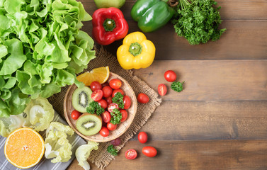 Fresh salad vegetables and fruit on wood background.