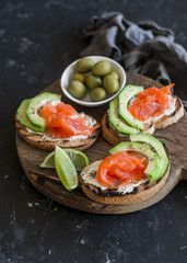 Delicious appetizers with wine - cream cheese, smoked salmon and avocado sandwiches and olives on a wooden board.