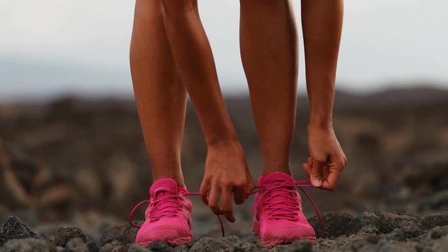 Running woman tying shoe laces going running - girl trail runner. Closeup of female legs and running shoes in action. Girl athlete fitness runner running fast outside in trail running shoes. 