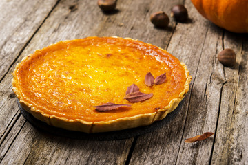 Pumpkin pie on the shabby wooden background with pumpkin, chestnuts and autumn leaves. Selective focus 
