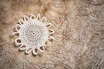 white crocheted handmade doily in a shape of the sun with copy space on a cement background,...