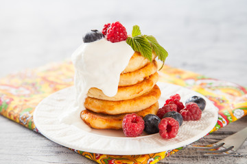 Summer cottage cheese pancakes on white plates on a  table with sour cream and berry, closeup, selective focus