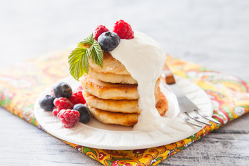 Summer cottage cheese pancakes on white plates on a  table with sour cream and berry, closeup, selective focus