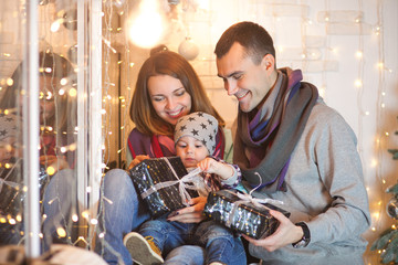 Family, mom dad and son near the window on Christmas Eve with lights and gifts