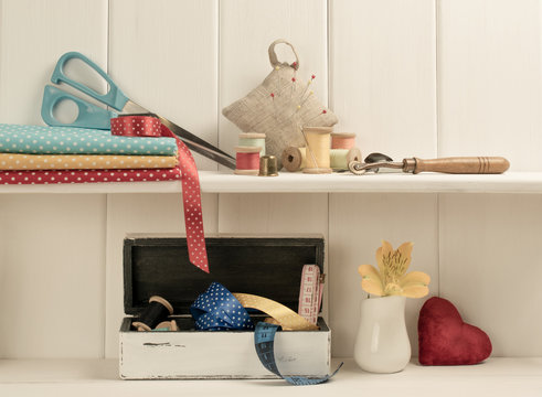 Set of tools for sewing and fabric lying on the wooden shelf. In