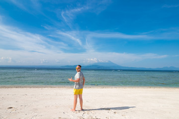 Fototapeta na wymiar Handsome young man with sunglasses against bright beach background and the blue Indian ocean. There is a volcano Agung on the background. Tropical island Nusa Lembongan, Indonesia.