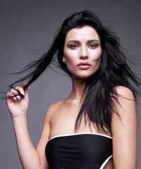 Portrait of a young brunette woman with long black streaming hair on gray background © Serg Zastavkin