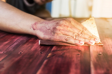 hand sanding and smoothing red wooden with sandpaper.