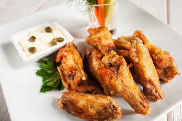 Close-up of fried chicken wings on white plate. Delicious golden grilled snacks served with creamy sauce. Junk fast food, fat concept