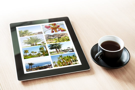 Tablet pc with vacation pictures gallery and cup of coffee on the table, Planning and booking travel idea