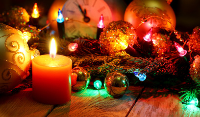 Fototapeta na wymiar New Year`s card with Christmas tree fir branches, midnight clock, burning candle, golden balls, garland lights on vertical old wooden desk table background. 