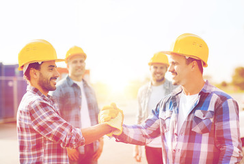 group of smiling builders shaking hands outdoors