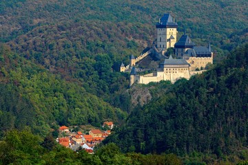 Obraz premium Gothic royal castle Karlstejn in green forest during autumn, Central Bohemia, Czech republic, Europe. State caste in with village in valley. Castle with tower in landscpae. Czech monument near Prague.