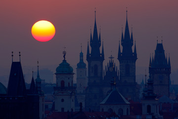 Fototapeta na wymiar Beautiful detailed sunrise view of Prague church towers. Early morning colours with old town. Twilight in historical city. Magical picture of tower with orange sun in Prague, Czech Republic, Europe.