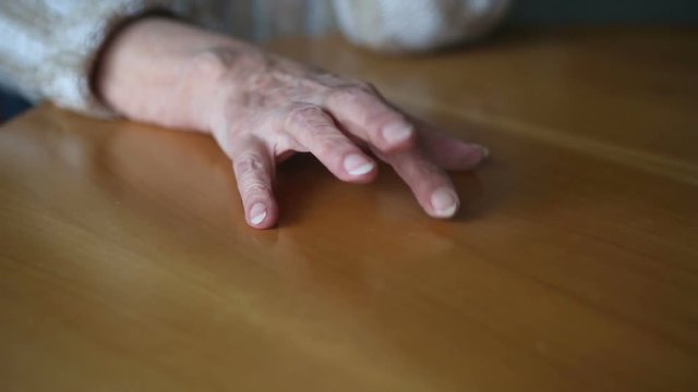 closeup of old woman’s hands tapping nervous on table
