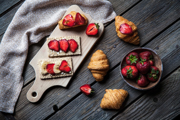 A delicious breakfast of strawberries and bread on wooden background. Fruit, food, sandwiches, cheese. Vintage style.