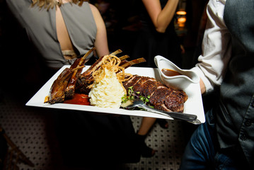 Waiter carries baked meet and sauce on square plate