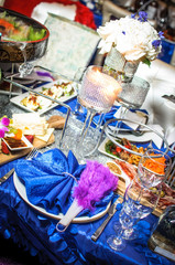 White candles decorated with crystals stand on blue dinner table