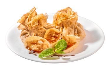 Traditional Romanian crepes with banana slices, hazelnut spread with cocoa and mint leaves decoration, on white plate and isolated on white background