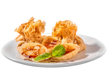 Traditional Romanian crepes with banana slices, hazelnut spread with cocoa and mint leaves decoration, on white plate and isolated on white background