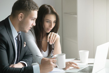 Young businessman and businesswoman sitting at the office desk, office workers looking at the...