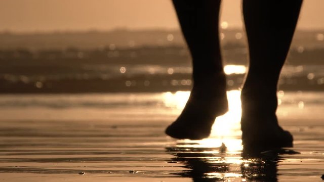 Low angle on sandy beach at sunset with barefooted person walking to the water's edge.