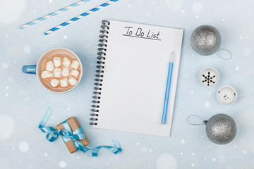 Cup of hot cocoa, gift, holiday decorations and notebook with to do list on blue vintage table from...