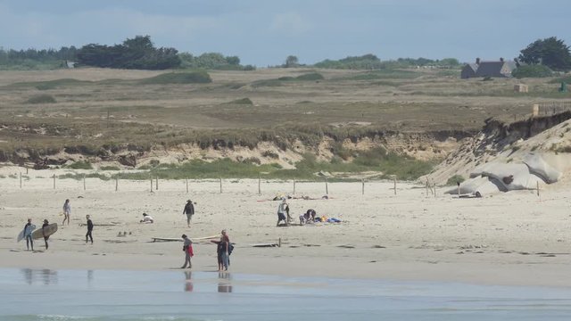 Shot from the sea towards the beach in Brittany, France. Sunbathers and surfers wander about on a sunny day.