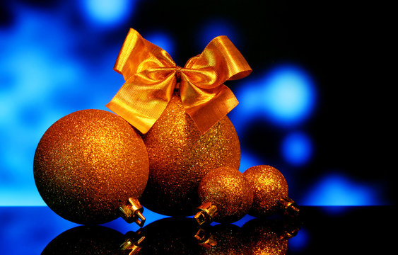 Christmas gold balls decorations with Bow of golden ribbons on a black mirror reflection surface and night blue bokeh lights background