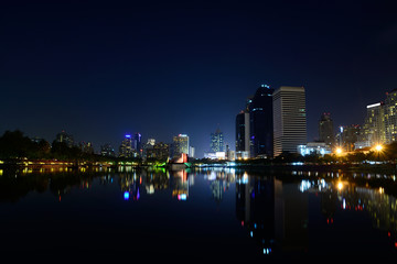 Fototapeta na wymiar Modern city view of Bangkok, Thailand. Cityscape with Commercial Building Beside Lake in Public Park with Reflection at Twilight or Night