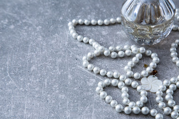 a strand of pearls and perfume on a stone background