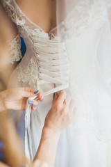Morning of young anonymous beautiful bride. Getting ready for wedding ceremony. Bridesmaid helping young bride to dress up bridal dress. Female hands with modern blue manicure. Vertical color image