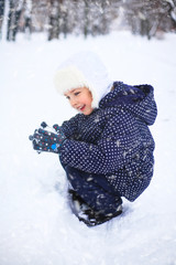 Small girl playing with snow in a park. The concept of childhood and the winter season.
