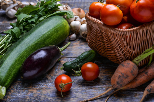 Harvest Vegetables: tomatoes, cucumbers, zucchini, eggplant, onion, garlic, arugula on the wooden background