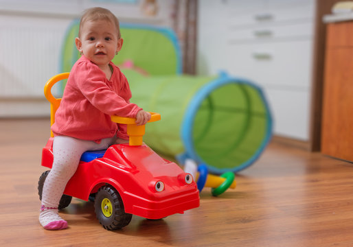 Little Child Girl Is Playing, Sitting On Red Toy Car And Driving It.