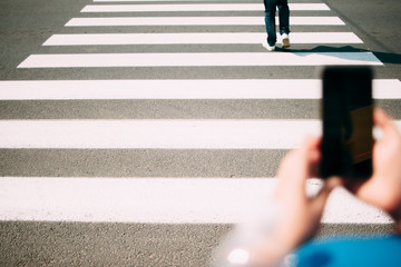 Pedestrian zebra close-up, smartphone on foreground. Photo of people crossing intersection on right...