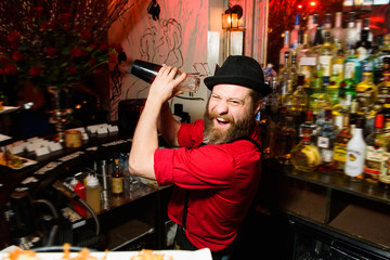 Laughing barman in red shirt makes a cocktail