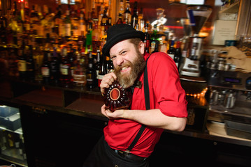 Funny waiter in red shirt holds bottle of whisky