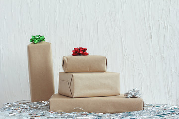 Stack of gifts in kraft paper with bow of green, red and silver colors. Plaster wall. Copy space, mock up