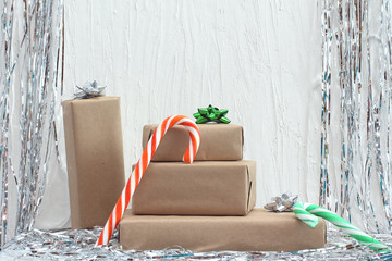 Stack of gifts in kraft paper with bow of green, red and silver colors. Tinsel on a white background Christmas candy cane. Plaster wall. Copy space, mock up