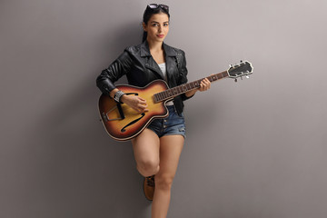 Young woman playing a guitar and leaning on a gray wall