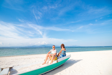 Obraz premium Happy honeymoon vacation at paradise. Couple relax on the white sand of beach, sitting in the old boat. Happy sea lifestyle. Young family, man and woman rest on the beach of ocean. Couple in love