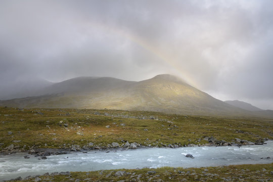 Rainbow forming in the rain clouds in autumn green landscape golden sunlight on mountains