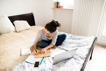 Beautiful young woman sitting on bed, working. Home office.