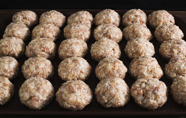 Lots uncooked meatballs on dark tray