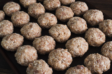 Lots uncooked meatballs on dark tray