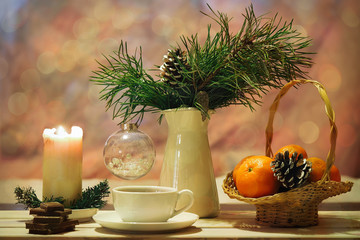 Holiday tea with chocolate. Branches of pine in a jar, Christmas transparent ball. Candle beige, white cup. Basket with bright tangerines and some chocolate