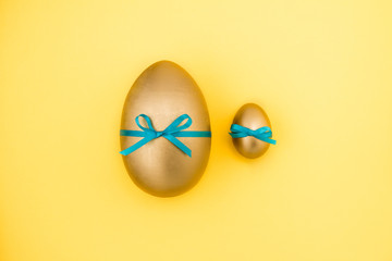 Golden Easter eggs with blue ribbon on yellow background. Easter concept
